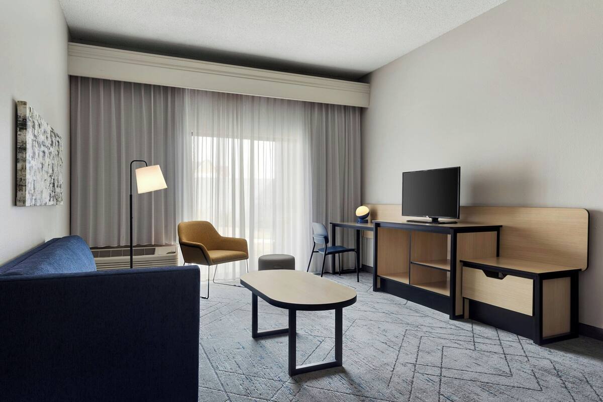 Una habitación de hotel con sofá, escritorio con televisor, lámpara y silla.