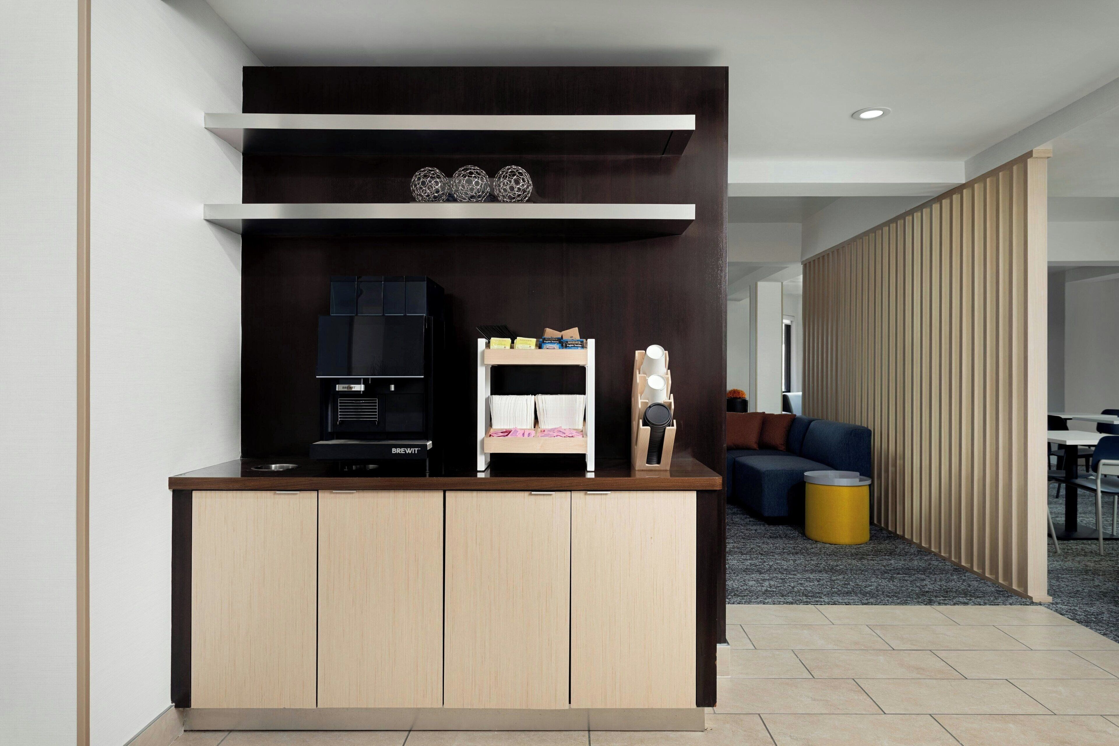 Un área de cocina moderna con cafetera, un pequeño rincón de estar con sofá y un mamparo.