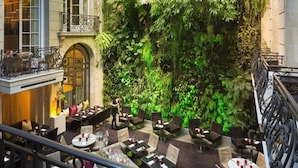 An indoor dining area with tables and chairs, a balcony with a railing, and a wall covered in greenery. - Pershing Hall (Paris)