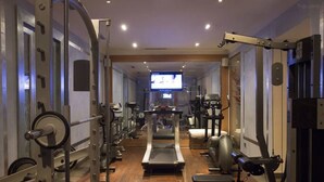 A gym with a treadmill, weight machines, and a television screen in the background. - Pershing Hall (Paris)