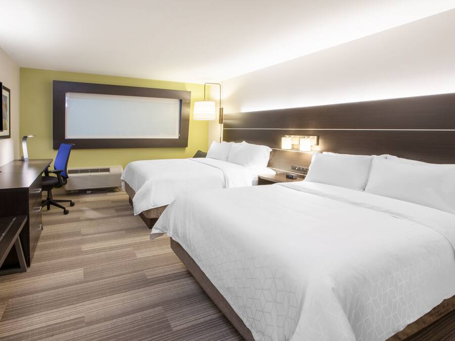 A hotel room with two beds, a desk, a chair, a TV, and a large window.