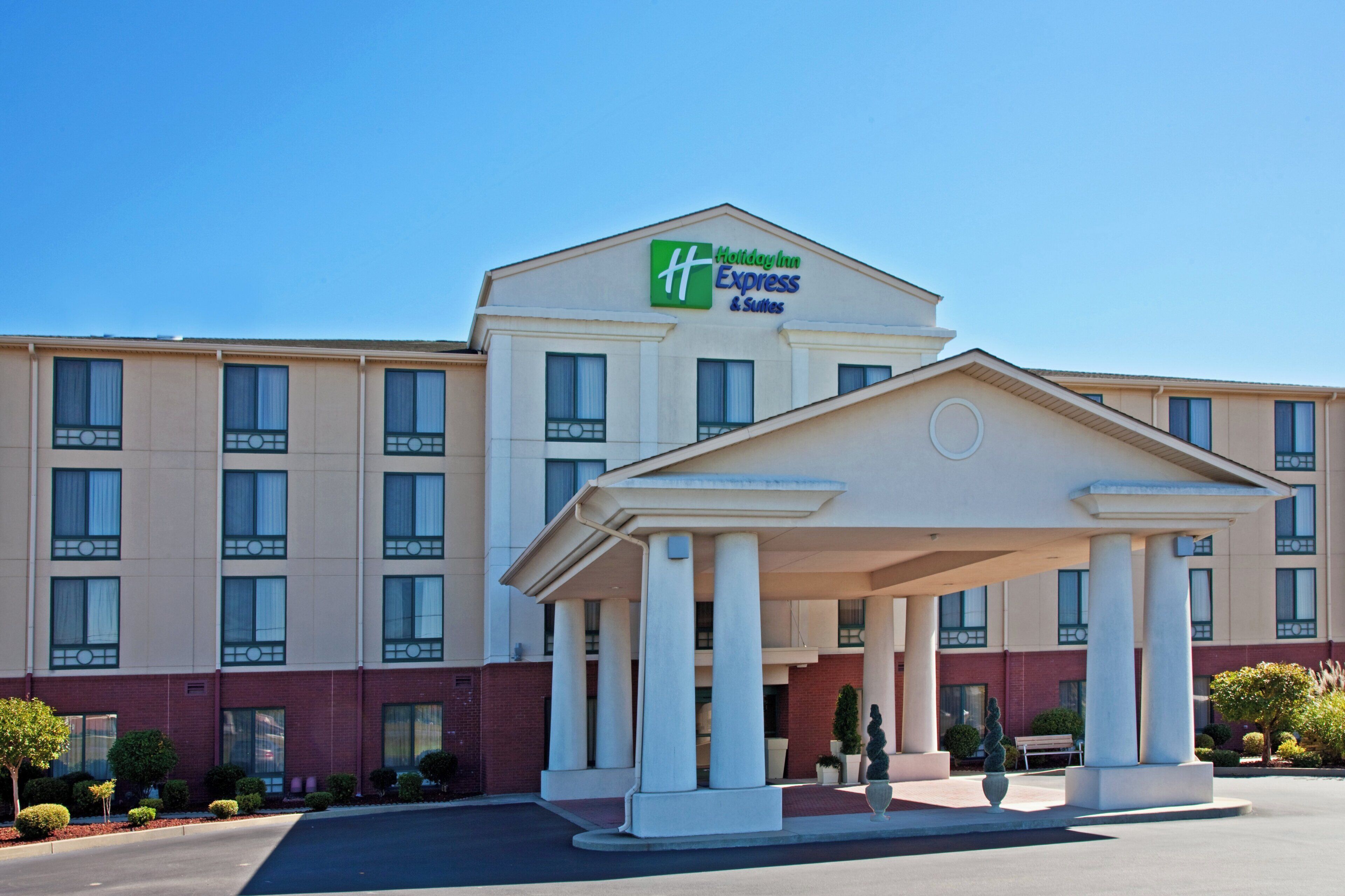 Een Holiday Inn Express & Suites gebouw met een centraal entree paviljoen, meerdere ramen en een heldere lucht.