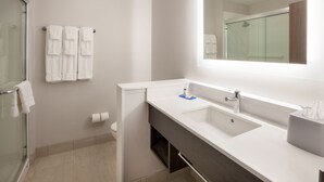 A modern bathroom with a glass shower enclosure, a white sink with a mirror above it, and a towel rack with multiple towels.