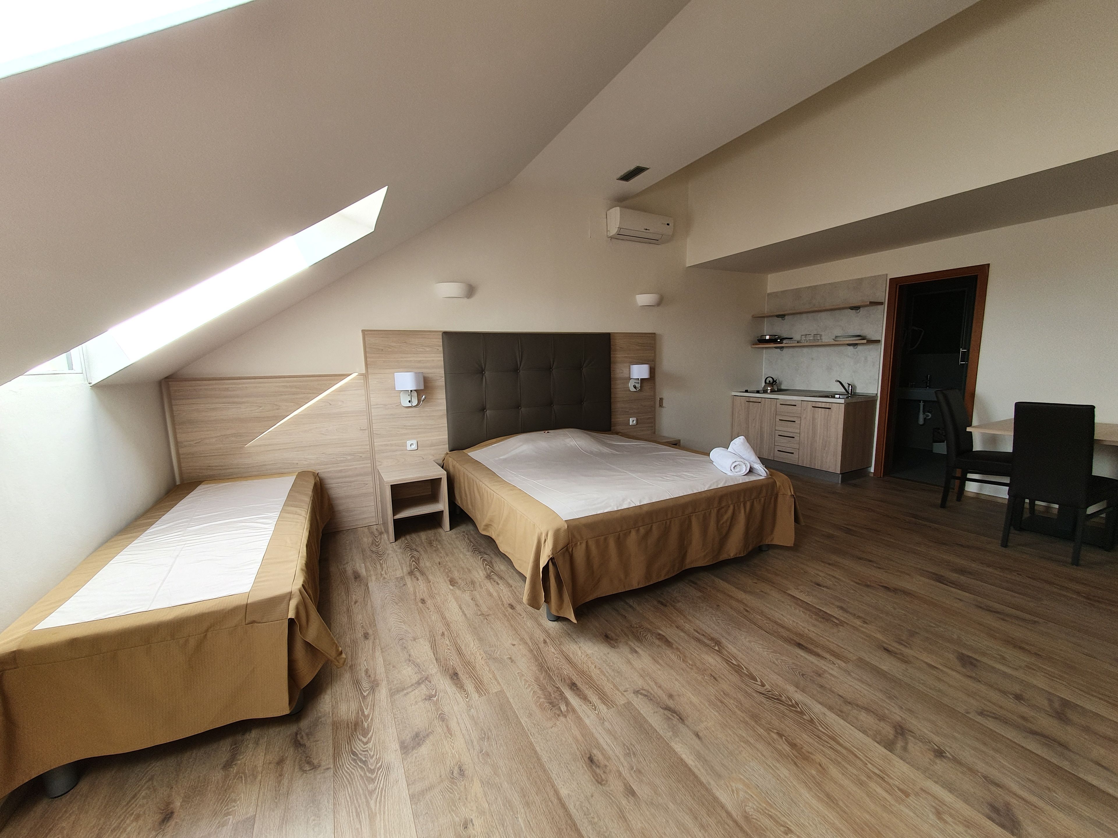 Hotellihuone, jossa on kalteva katto, sänky, työpöytä, tuoli, pieni keittiö ja kylpyhuone.