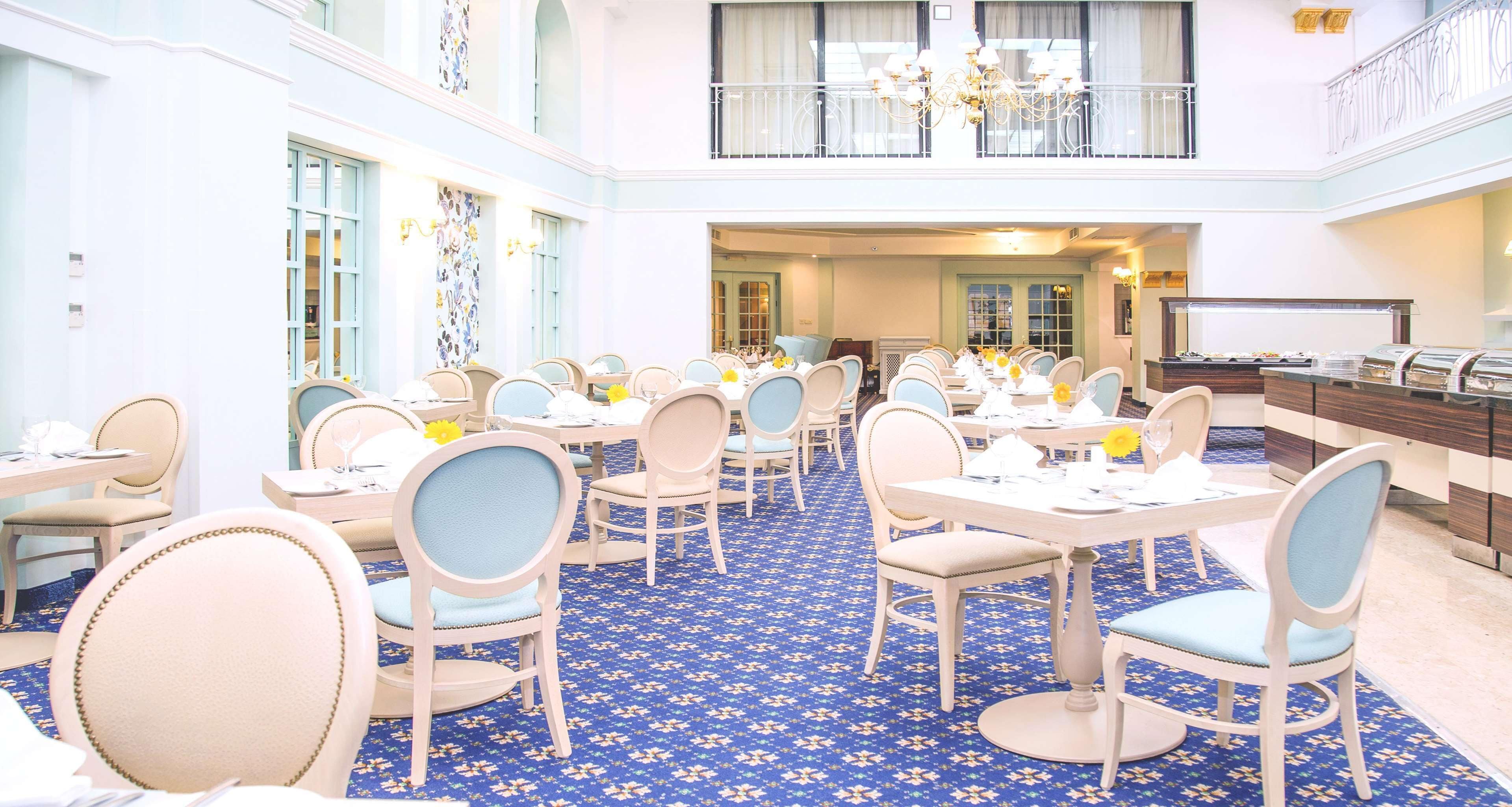 A spacious dining area with multiple tables and chairs, a buffet on the right, and a balcony with a railing.