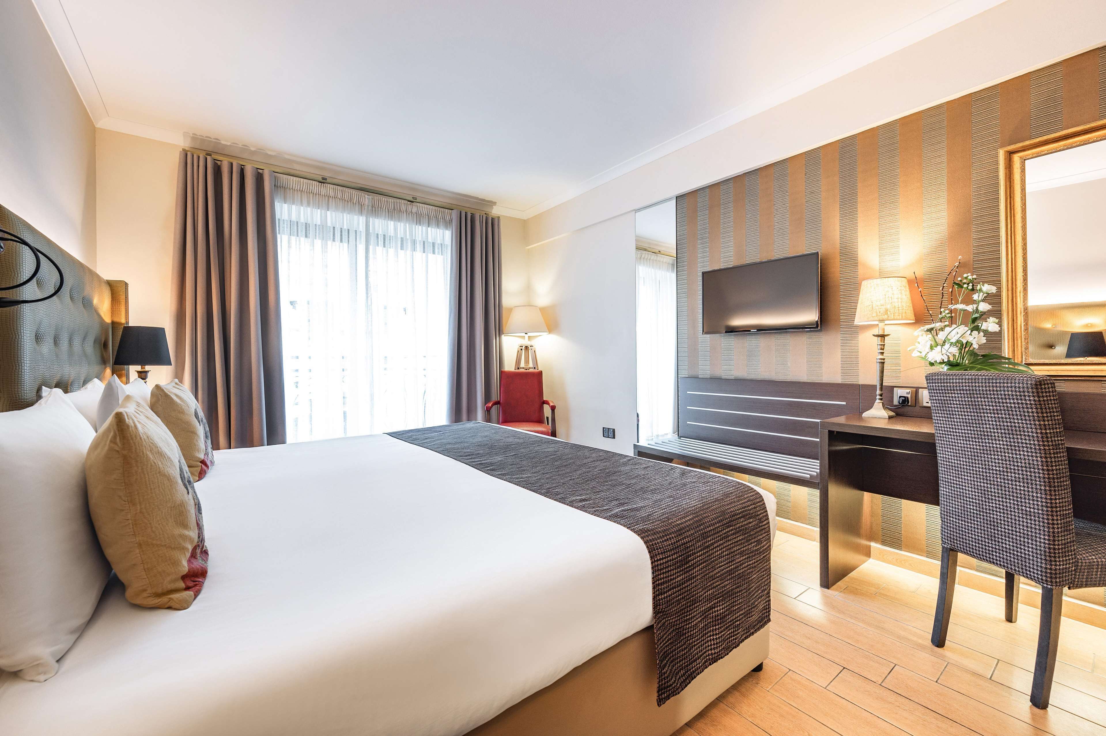 Habitación de hotel con una cama grande, un escritorio, una silla, un televisor y una ventana con cortinas.