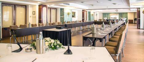 A conference room with long tables, chairs, and a stage area.