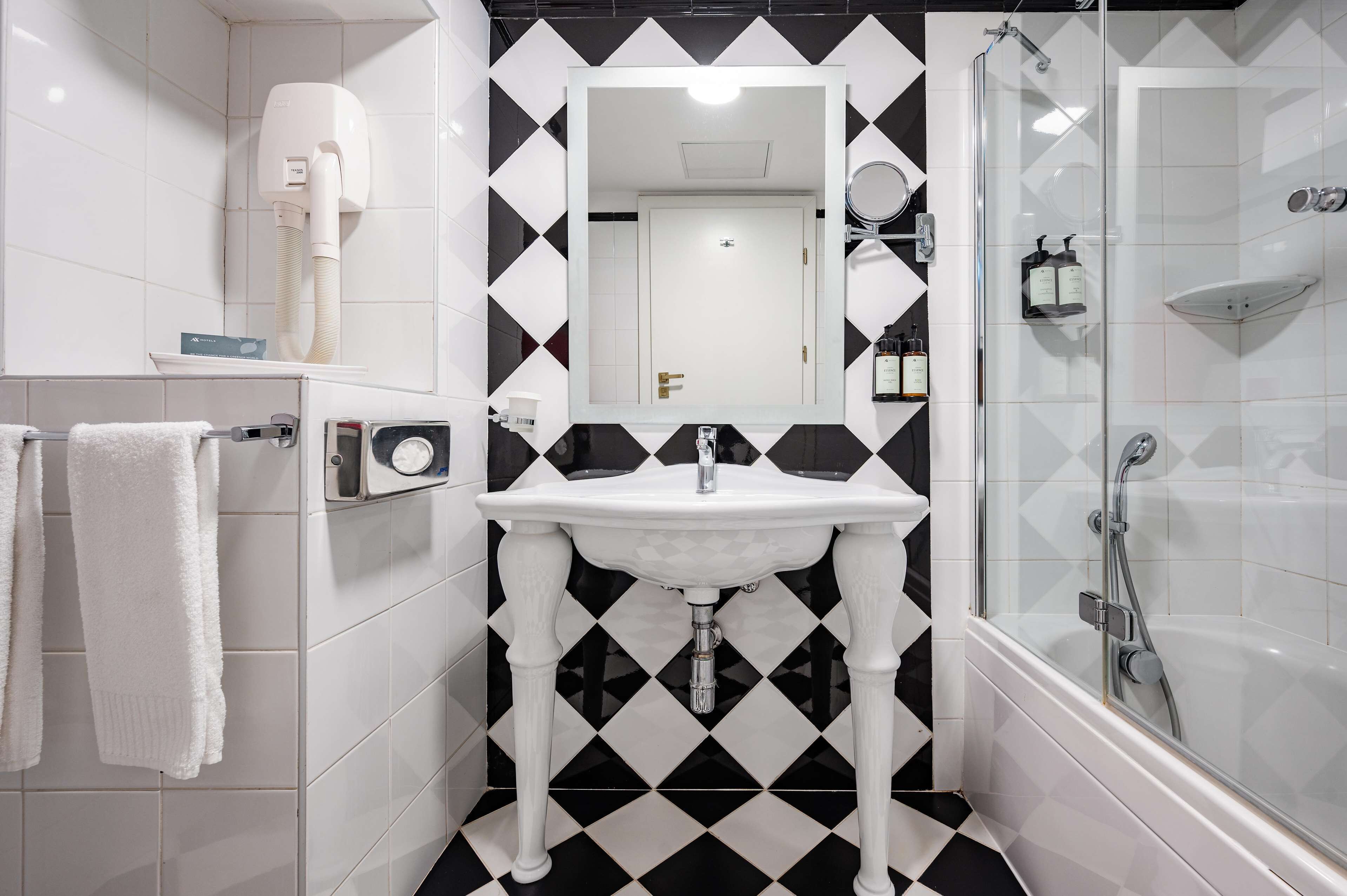 A bathroom with a white sink, black and white tiled walls, a glass shower enclosure, and a towel rack with a white towel.