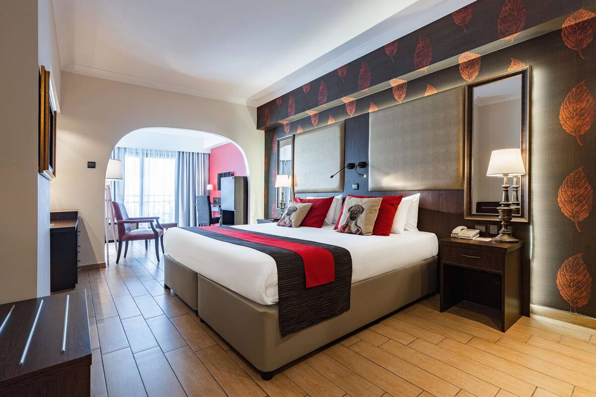 Une chambre d’hôtel avec un grand lit, un bureau, une chaise, une table de chevet et un miroir.