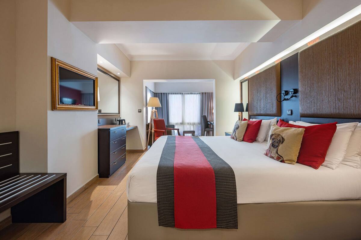 Une chambre d’hôtel avec un grand lit, un bureau, une chaise, une commode et un miroir.