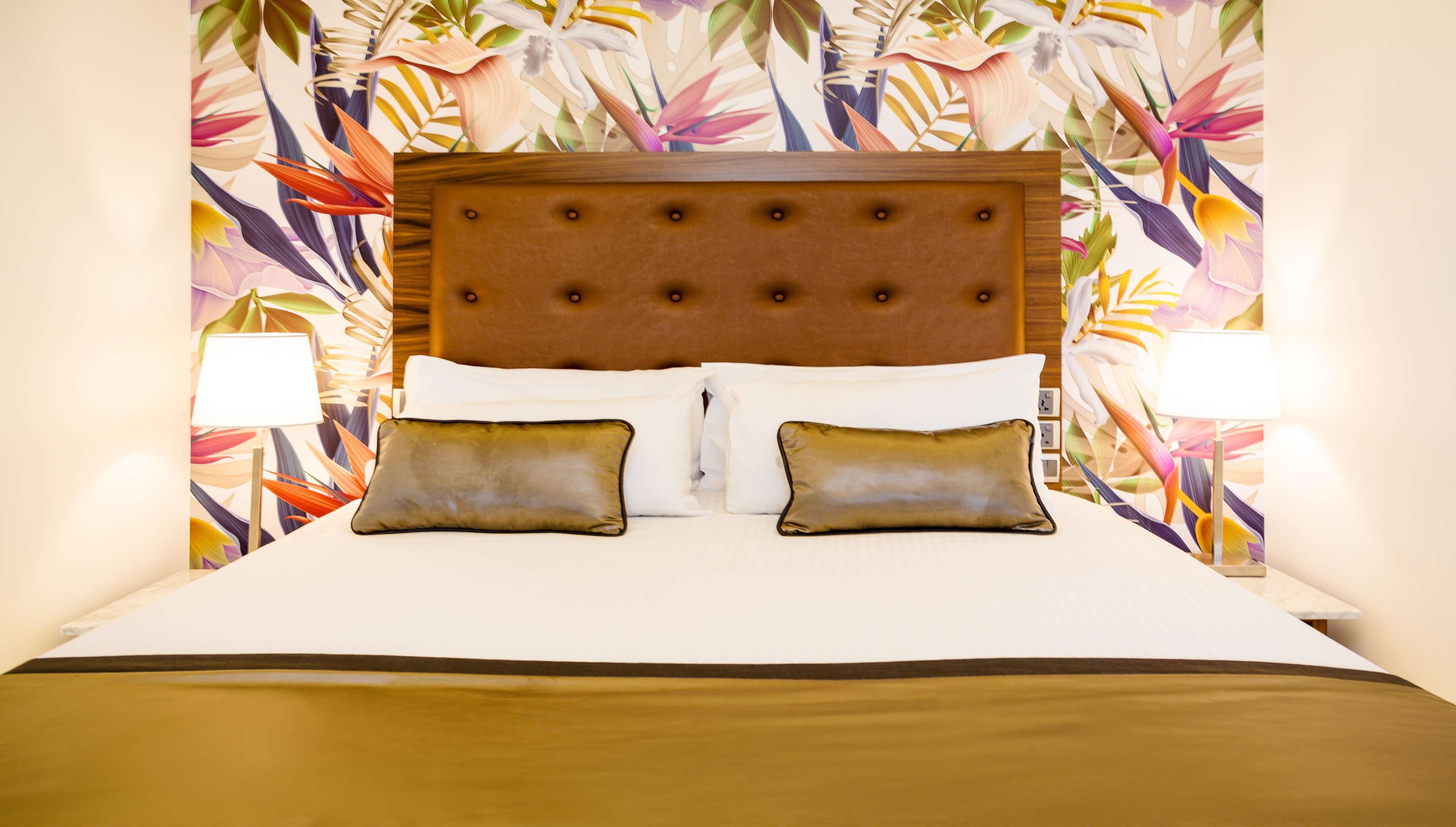 A hotel room with a large bed, two pillows, a wooden headboard, and a floral wallpaper.