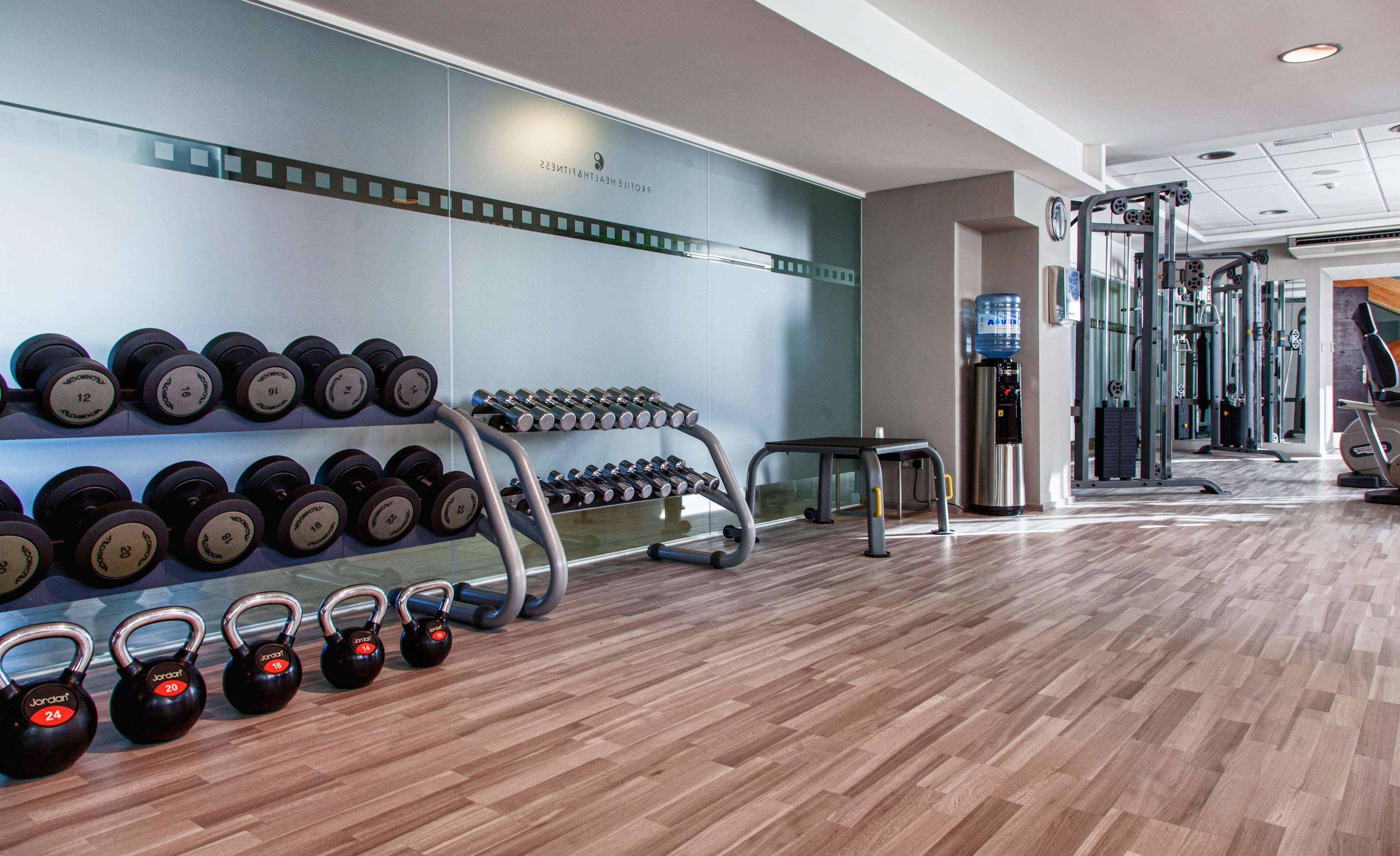 Une salle de sport équipée de matériel de musculation, notamment des kettlebells et des haltères, ainsi qu’un distributeur d’eau.
