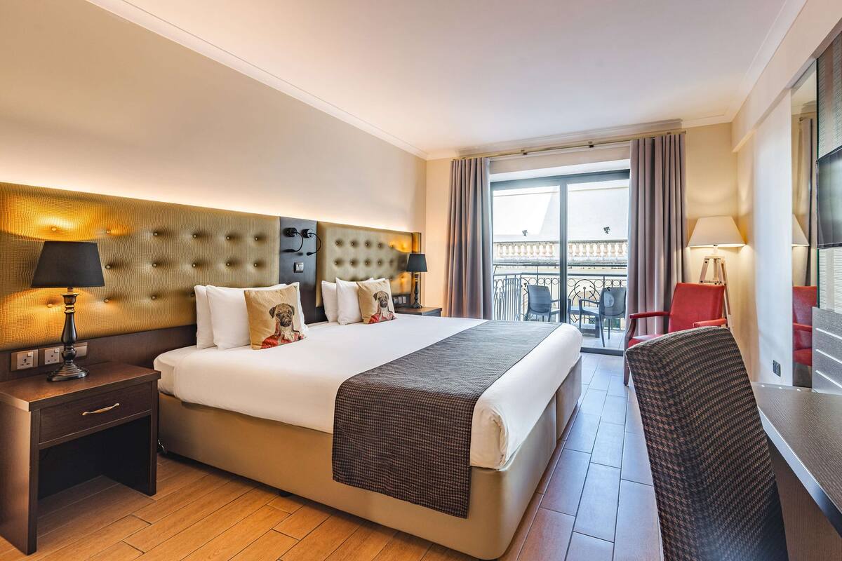Une chambre d’hôtel avec un grand lit, une table de chevet, un bureau et un balcon avec vue.