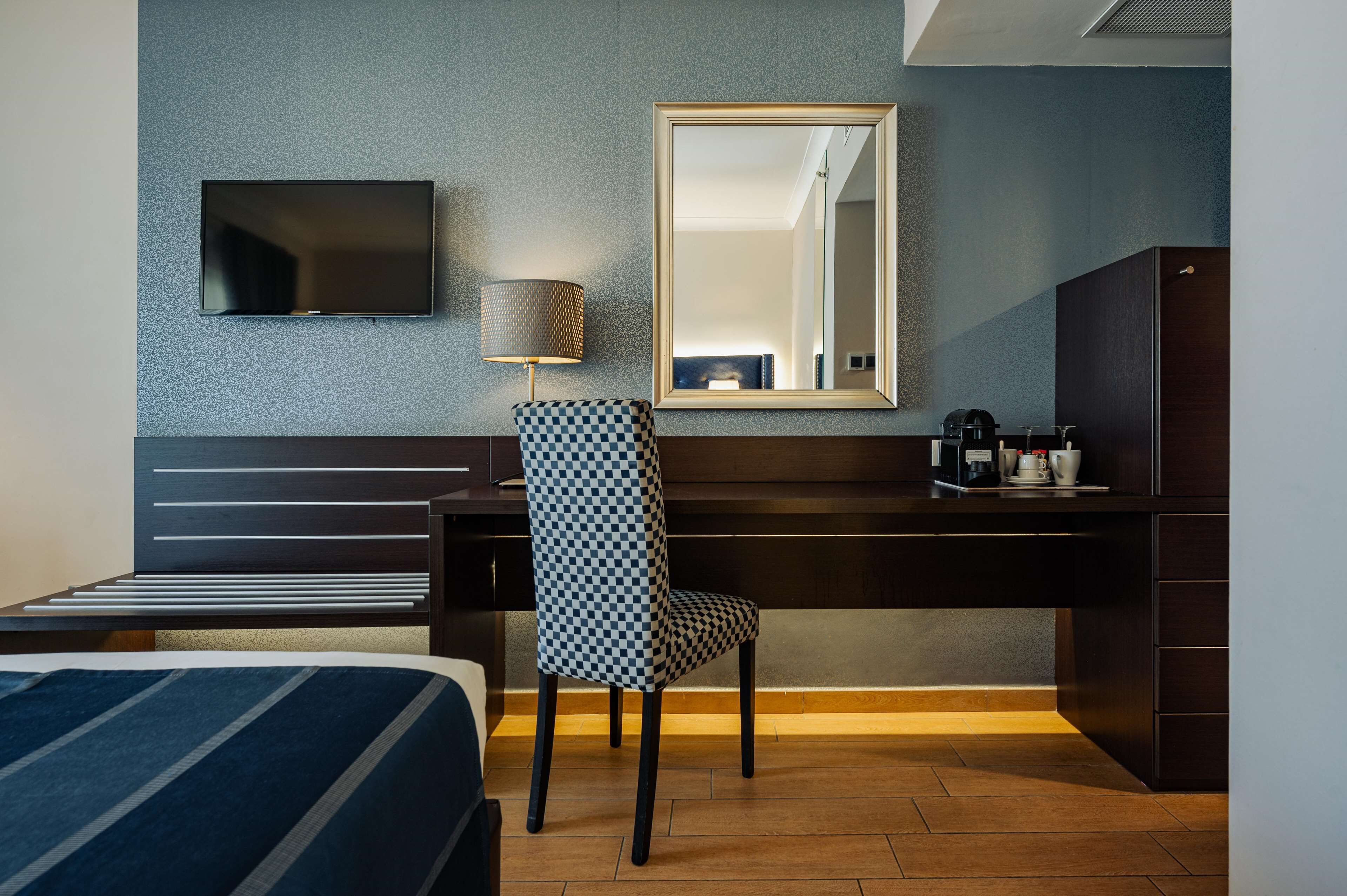 Habitación de hotel con cama, escritorio con silla, televisión, espejo y cafetera.