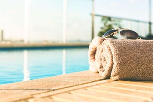 Zona junto a la piscina con toallas y gafas de sol, vista despejada de la piscina y un puente al fondo.