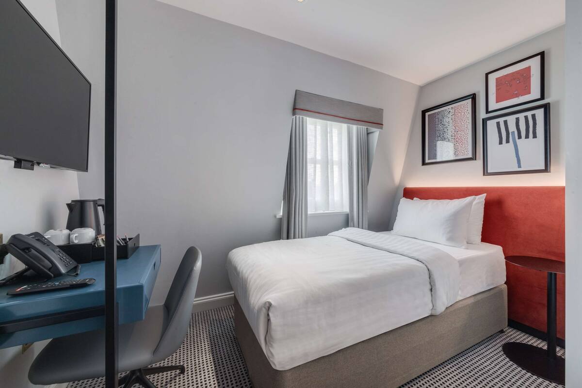 Hotellihuone, jossa on sänky, työpöytä, tuoli ja televisio.