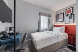 A hotel room with a bed, desk, chair, and a TV.