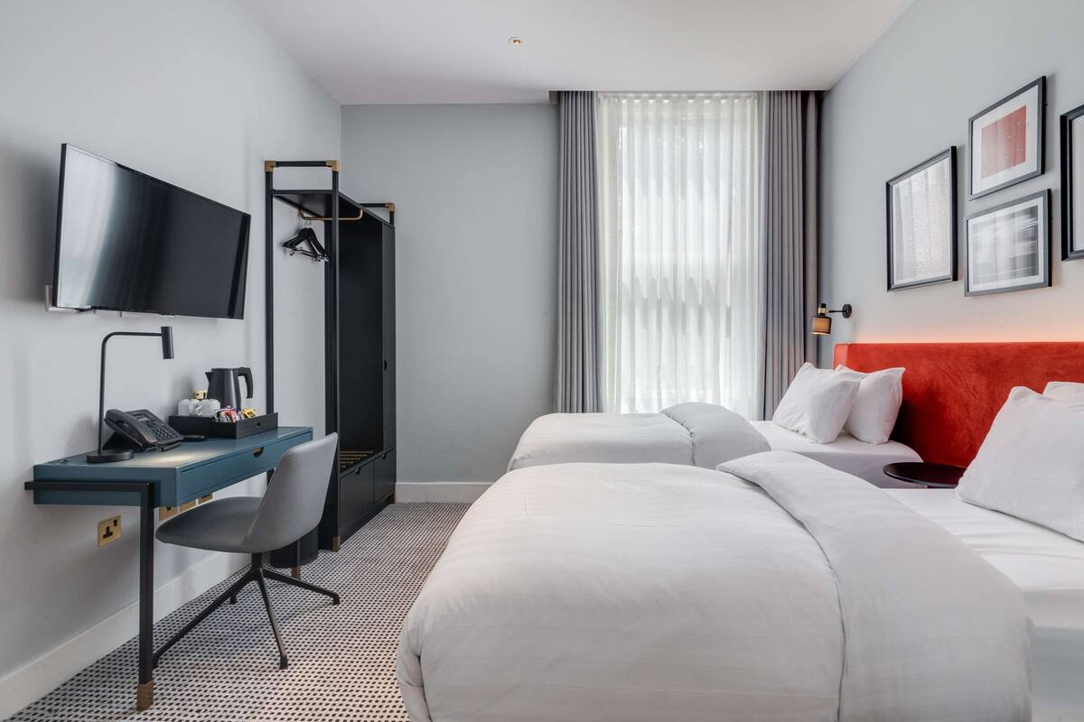 Hotellihuone, jossa on sänky, työpöytä tuolilla, televisio ja vaatekaappi.