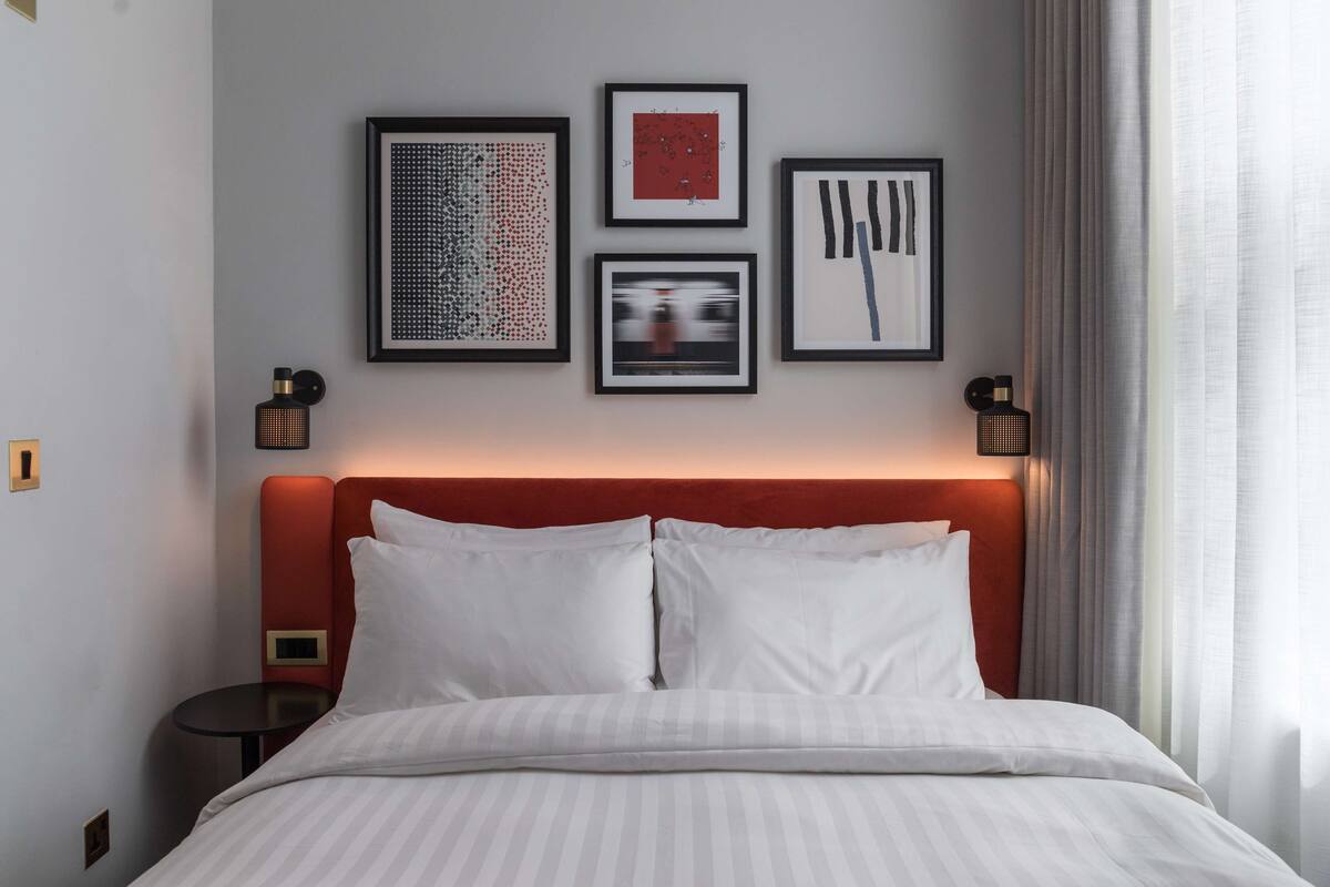 Hotellihuone, jossa on sänky, pyöreä pöytä ja seinällä kolme kehystettyä taideteosta.