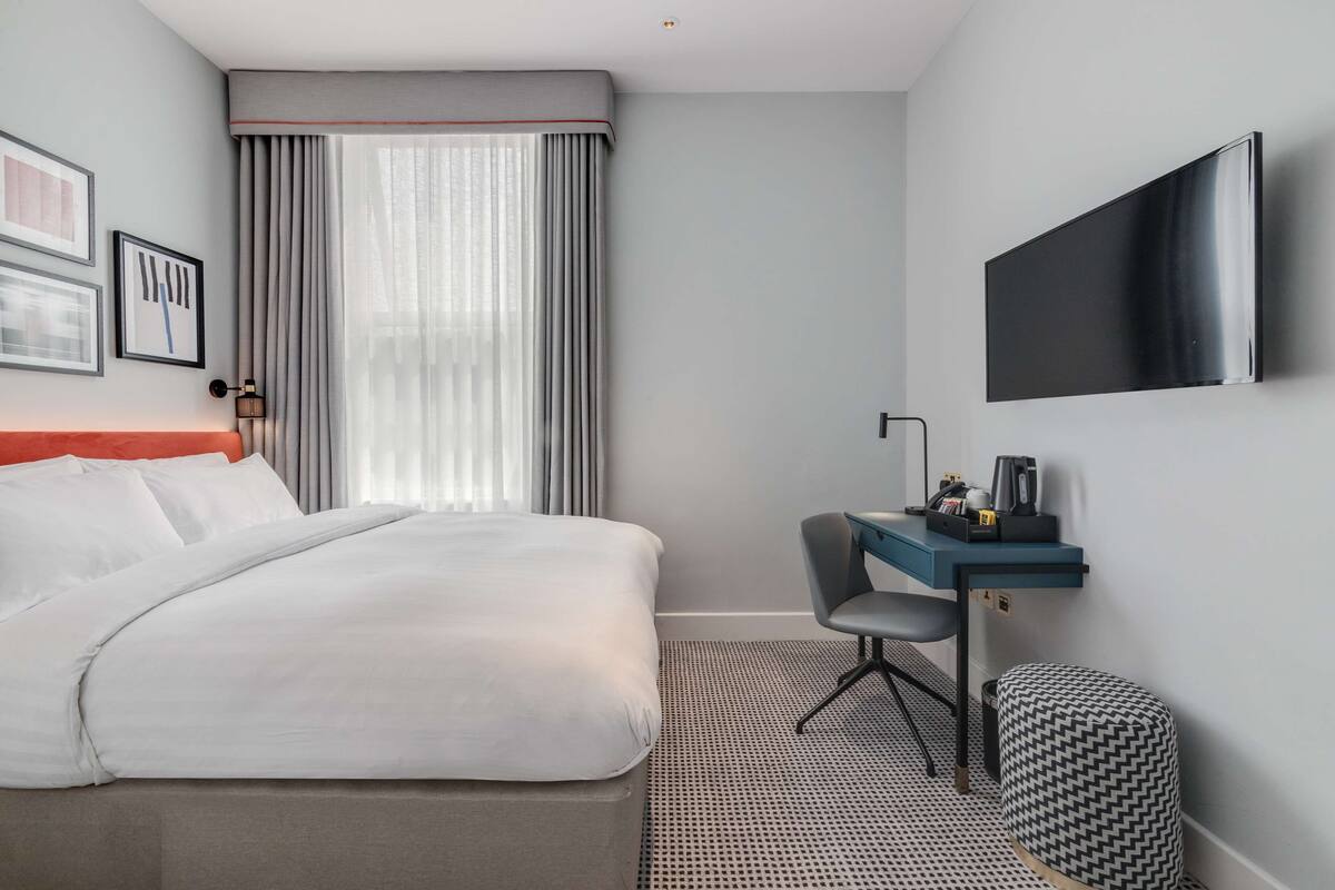 Hotellihuone, jossa on sänky, työpöytä, tuoli, televisio ja ikkuna, jossa on verhot.