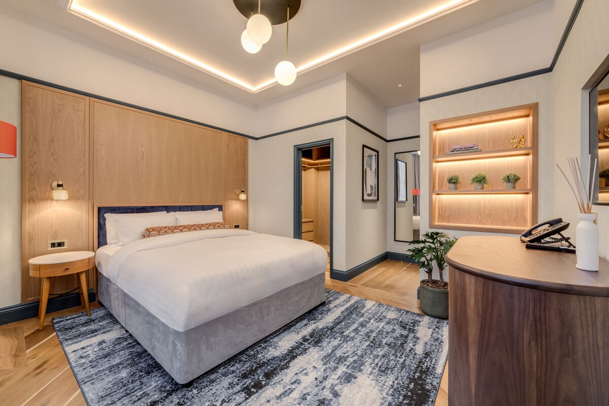 A modern hotel room with a large bed, bedside tables, a desk, and a built-in vanity with a mirror.