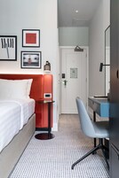 A hotel room with a bed, a desk, a chair, a small table, and a door.