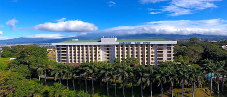 Ein mehrstöckiges Hotel mit flachem Dach und einer Beschilderung mit dem Schriftzug "BARCELÓ SAN JOSE". Es ist von üppiger Vegetation und Palmen umgeben.