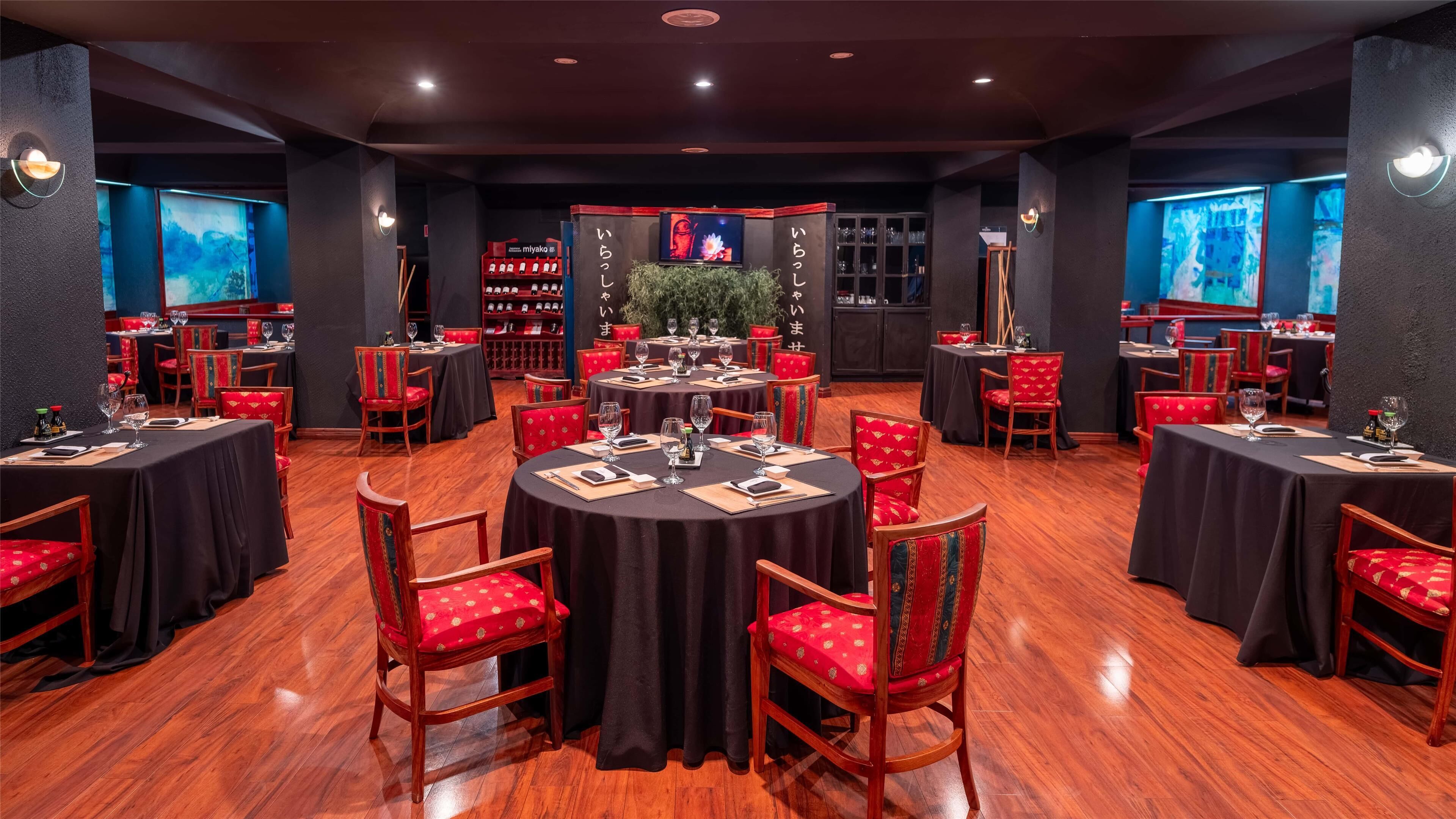 Un restaurante con mesas redondas, sillas tapizadas en rojo y manteles negros.