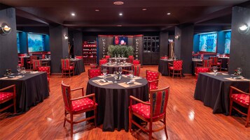 Un restaurante con mesas redondas, sillas tapizadas en rojo y manteles negros.