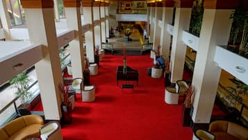 Un vestíbulo de hotel con alfombra roja, varias zonas de estar y plantas en macetas.