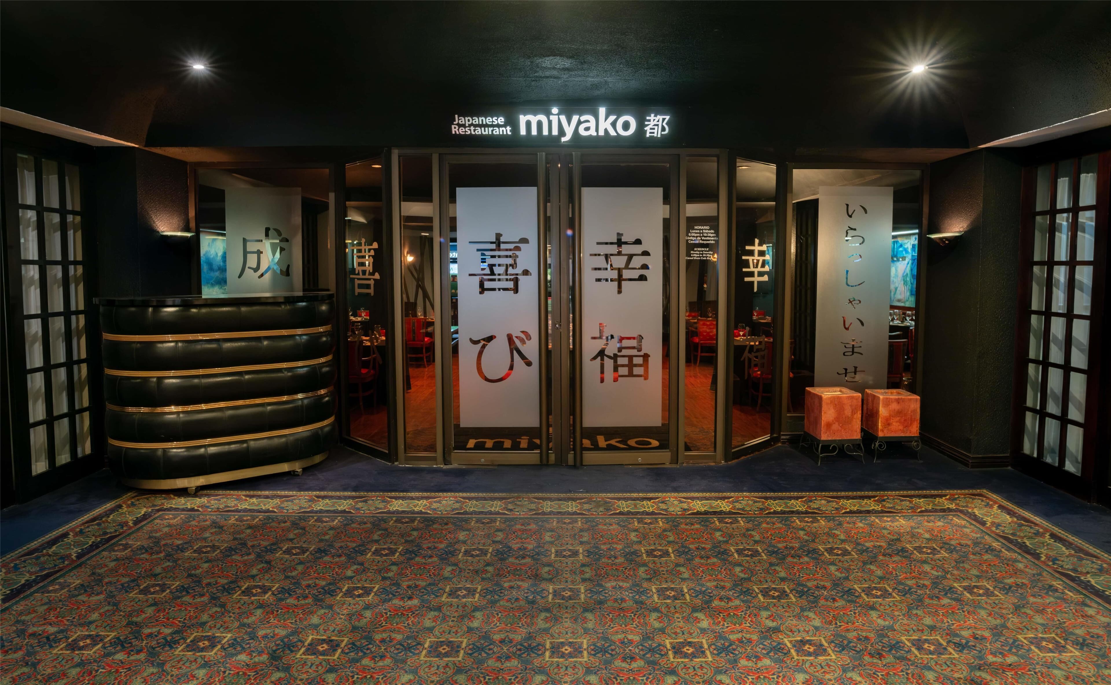 A Japanese restaurant entrance with a traditional design, featuring a patterned carpet and a large decorative stool.
