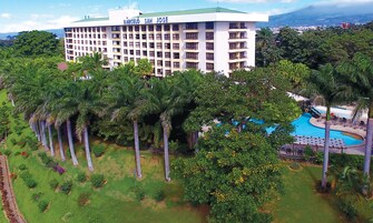 A large hotel with multiple floors and balconies, surrounded by lush greenery and a swimming pool.