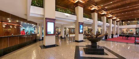 A spacious lobby with a high ceiling, polished tile flooring, and a reception desk.