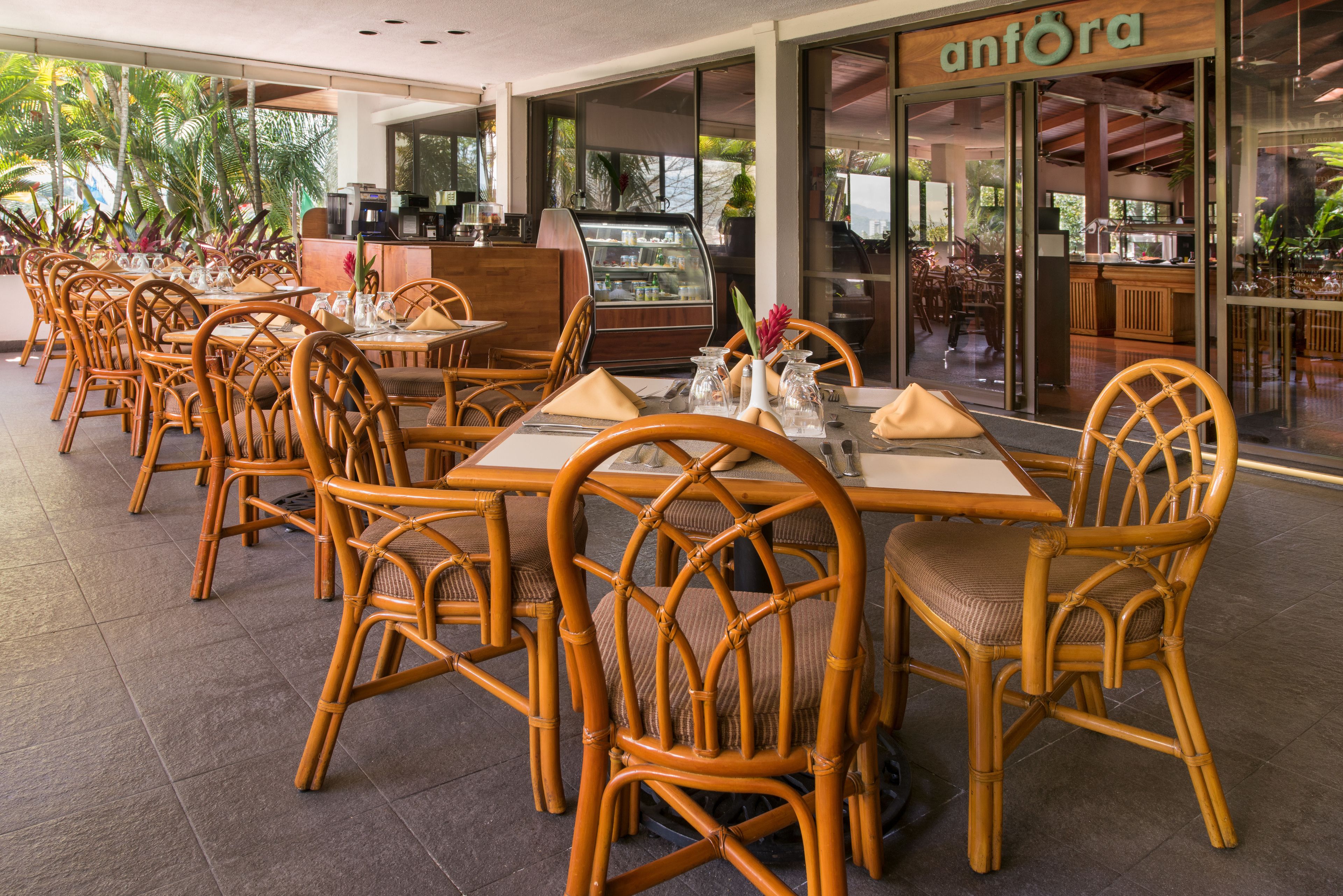 A restaurant with wicker chairs and tables, a coffee bar, and a view of the outdoors.