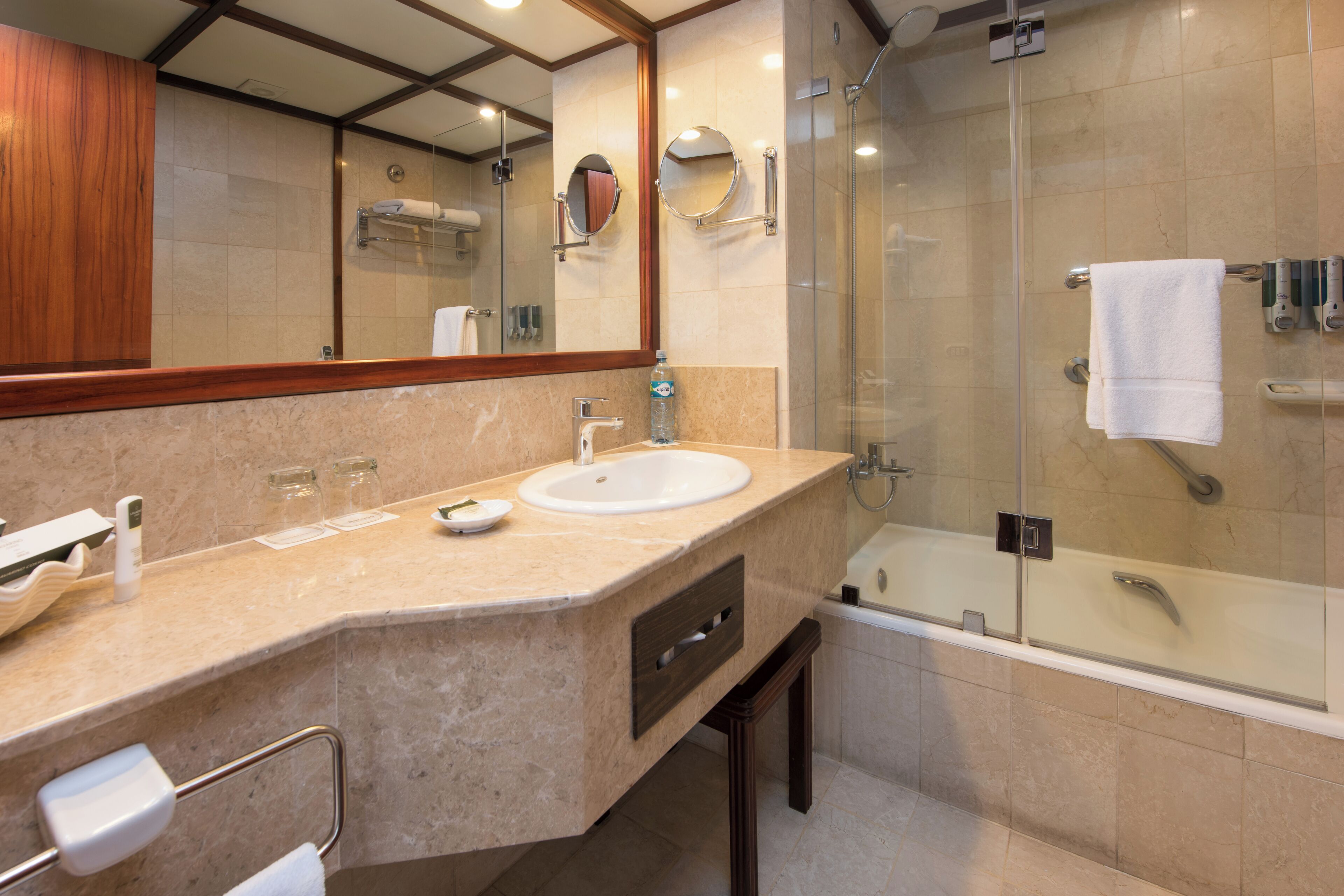 Un baño moderno con lavamanos de mármol, ducha con mampara de vidrio y un espejo grande.