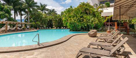 A pool area with lounge chairs, palm trees, and a building in the background.