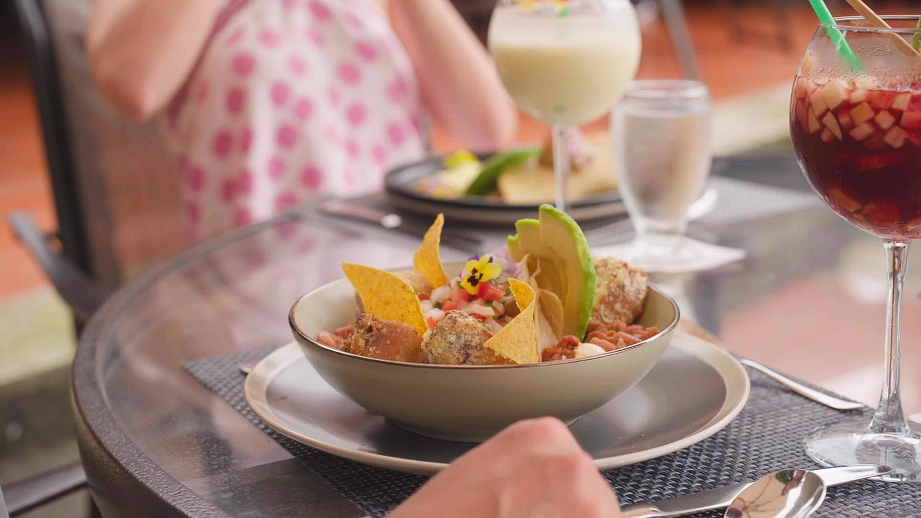 Un bol de nourriture, accompagné de chips de tortillas et d’une boisson, est posé sur une table.