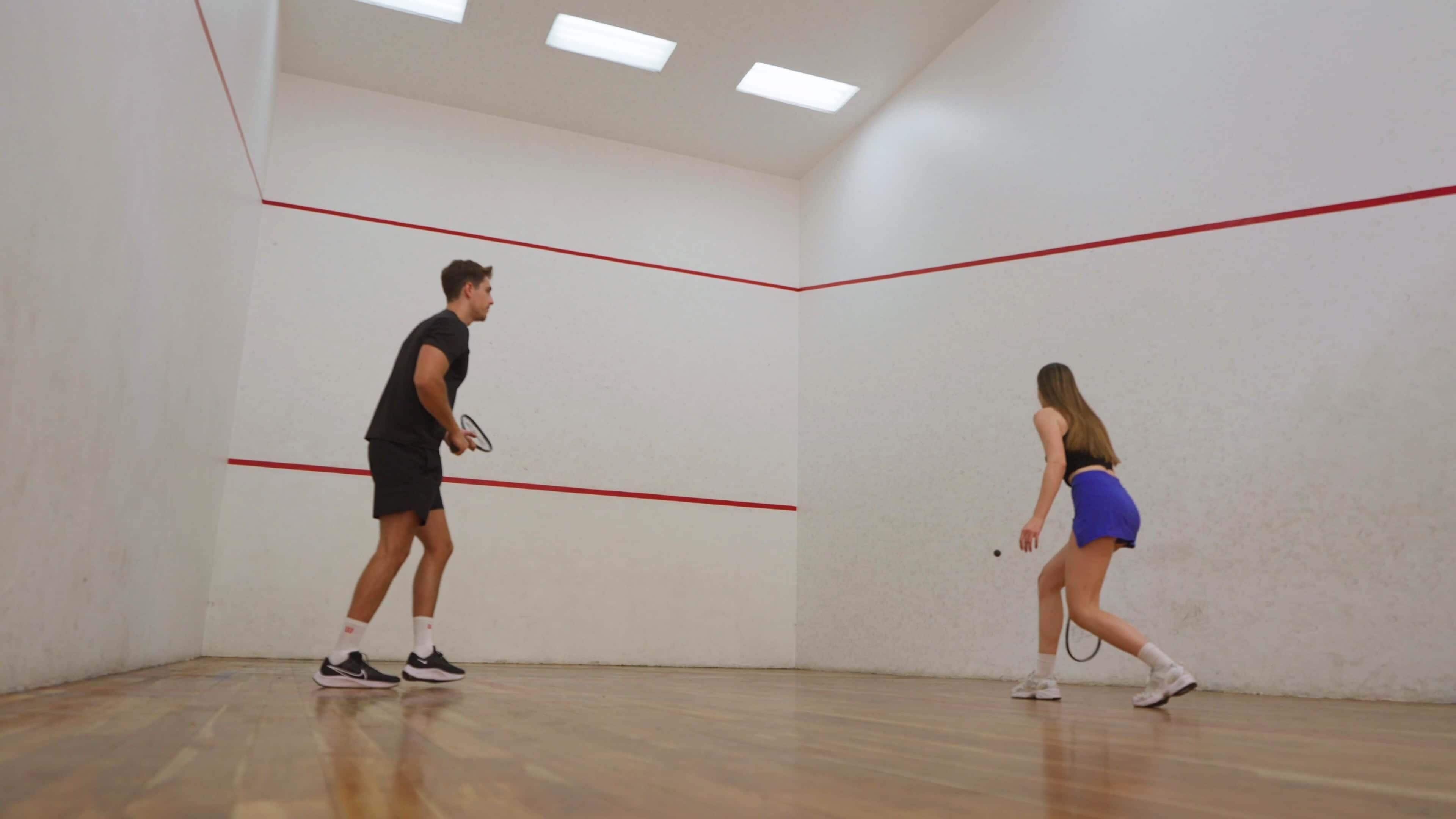 A squash court with wooden flooring and red boundary lines.