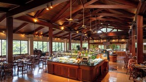 A spacious dining area with wooden ceiling beams, large windows, and a buffet setup. - Barceló San José (San José)
