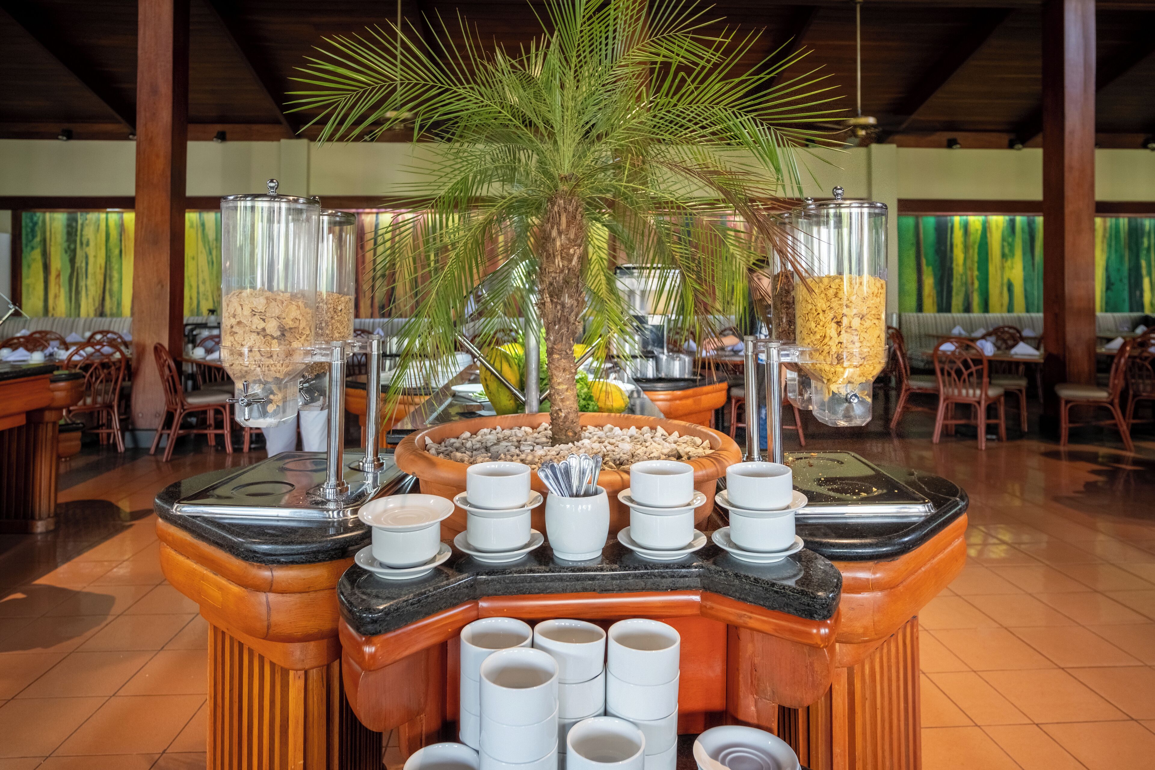 Un buffet disposé autour d’un grand palmier central, avec différents récipients et plats de service.