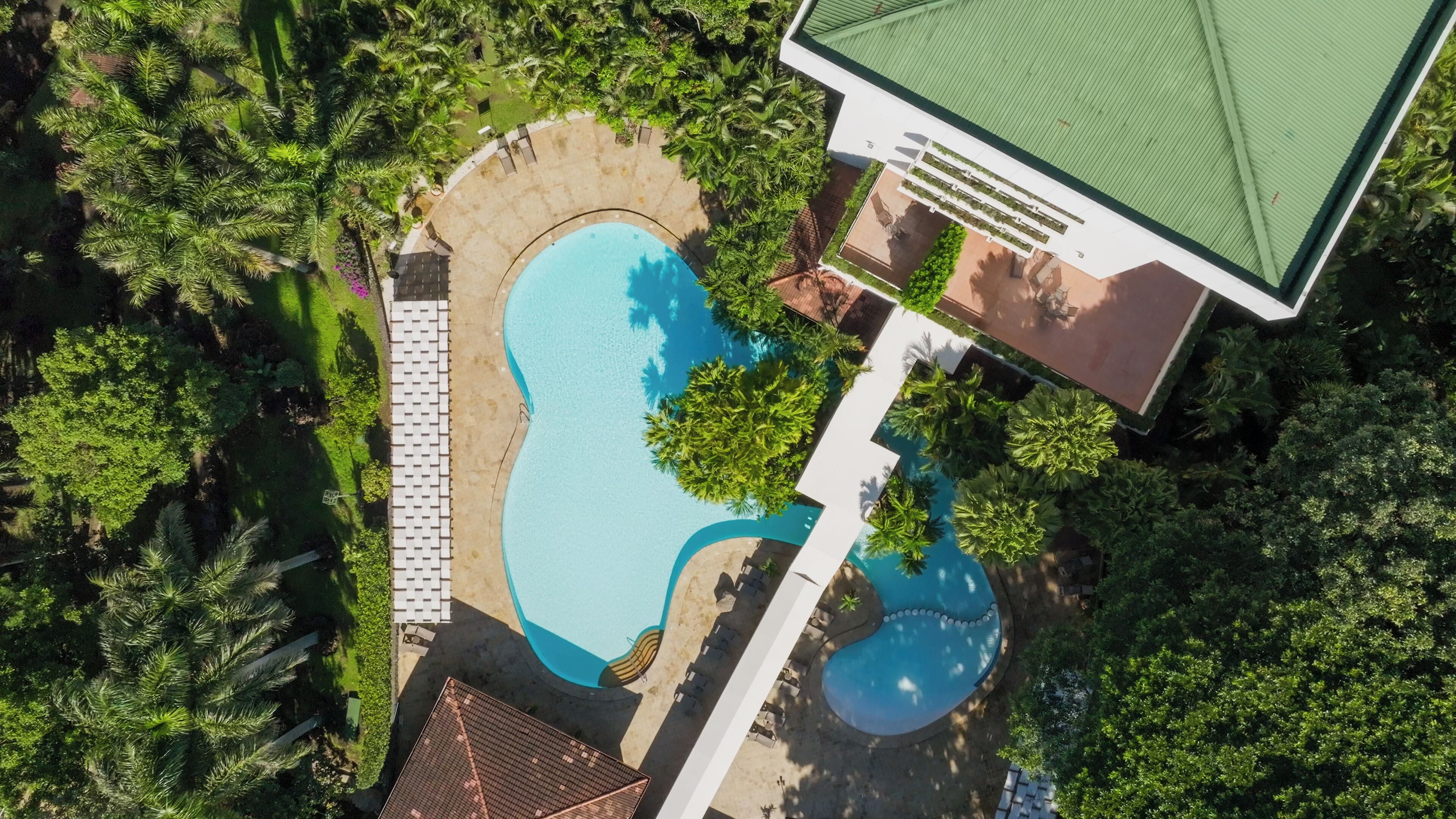 Vue aérienne d’un complexe hôtelier doté d’une grande piscine, d’espaces de détente et d’une végétation luxuriante.