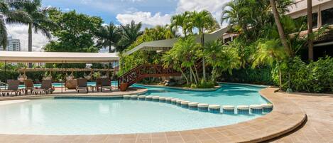 A swimming pool with a stone border, lounge chairs, and a covered seating area.