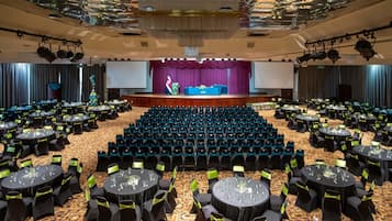 A large conference room with rows of tables and chairs, a stage with a flag, and a large screen.
