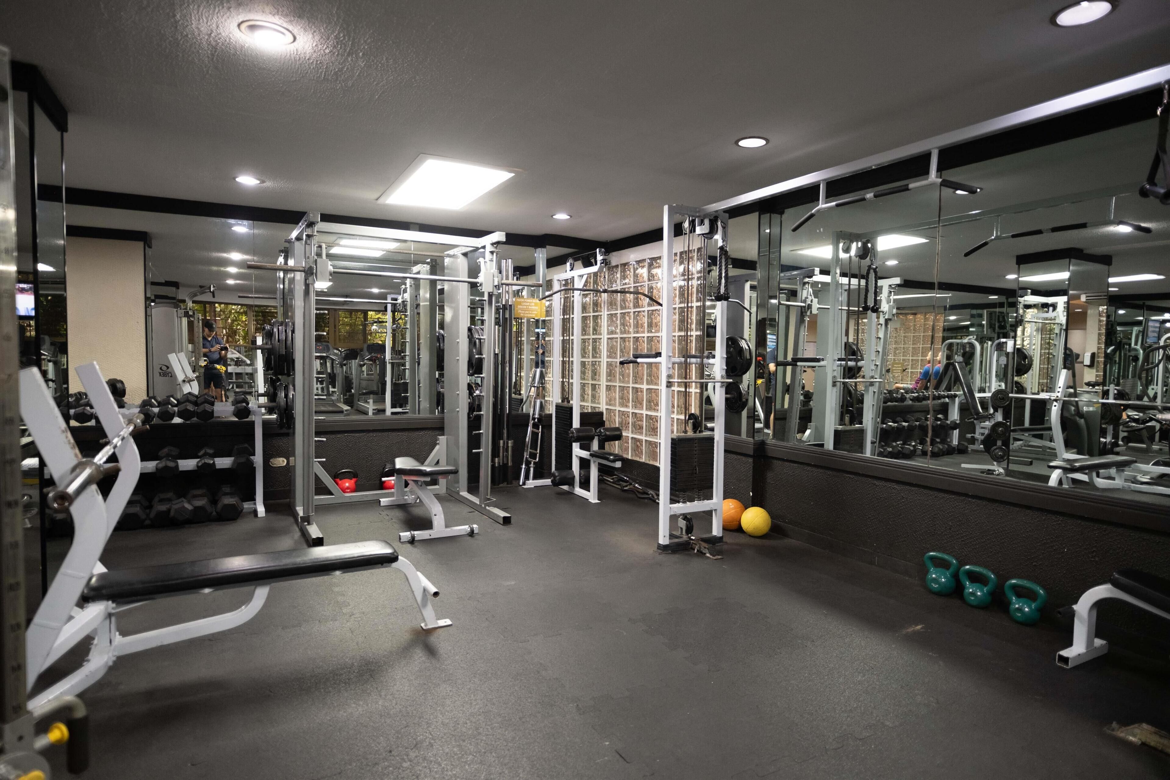 A gym with various exercise equipment, including dumbbells, kettlebells, and a bench.