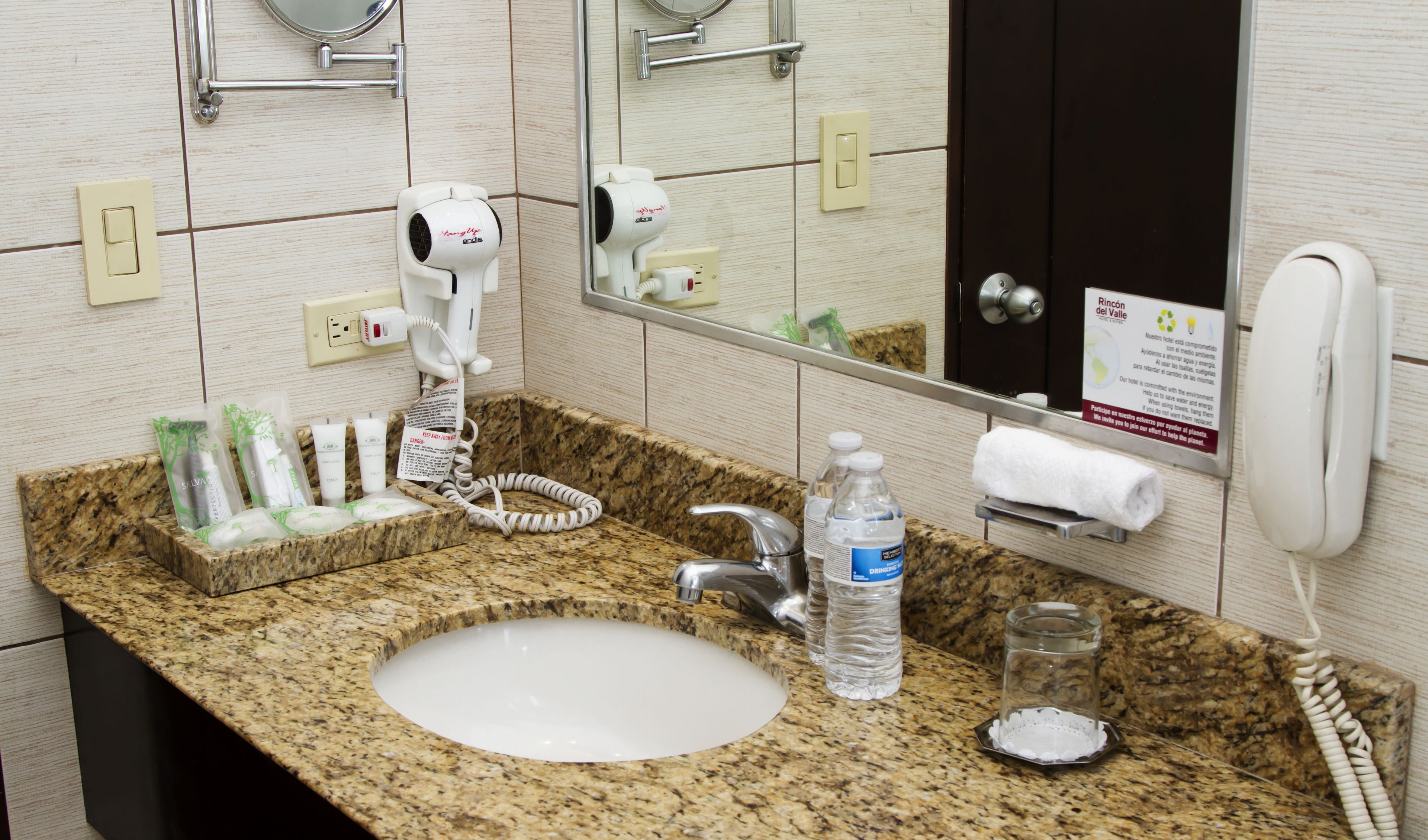 A bathroom with a granite countertop, a sink, a hairdryer, a mirror, and a towel rack.