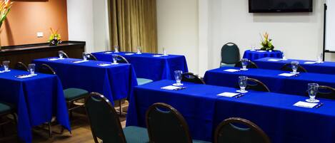 Un salón de conferencias con varias mesas cubiertas con manteles azules, equipado con sillas y vasos de agua.