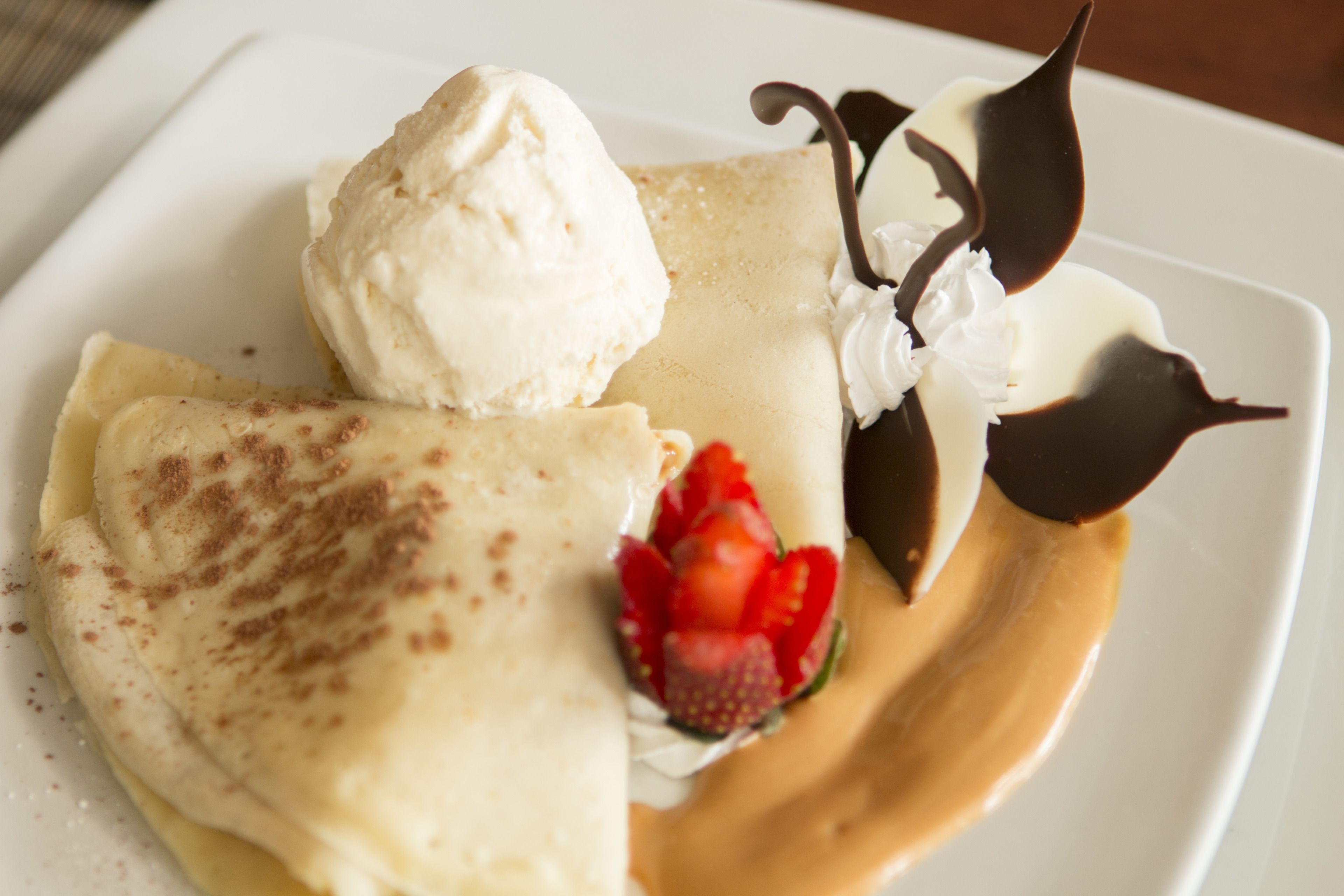 A dessert plate with crepes, ice cream, whipped cream, chocolate sauce, and a strawberry.
