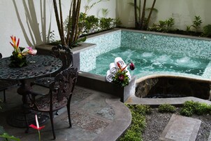Un área de piscina con borde de baldosas, una pequeña cascada y una mesa con sillas.