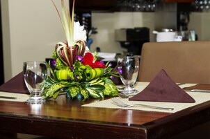Una mesa de comedor adornada con un centro de mesa floral, dos copas de vino y un mantel individual morado.