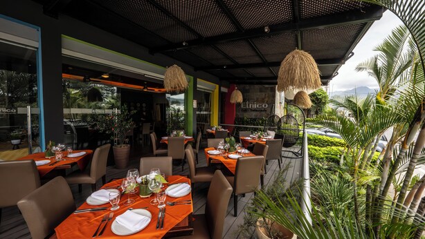 Un restaurante al aire libre con mesas dispuestas para comer, rodeado de follaje y vistas de la ciudad.